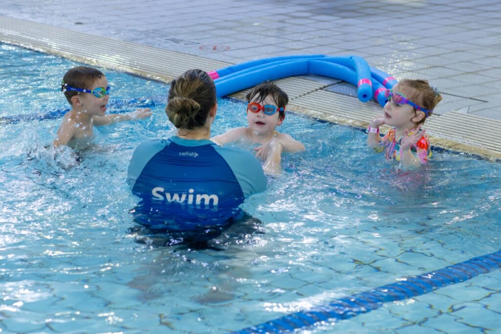 Swim teacher in the pool with three young children in goggles during a group lesson